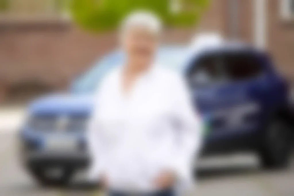 Ein Fahrlehrer mit weißem Hemd steht neben einem Fahrzeug, mit blauen Details im Hintergrund, während die Situation im Auto betont wird.